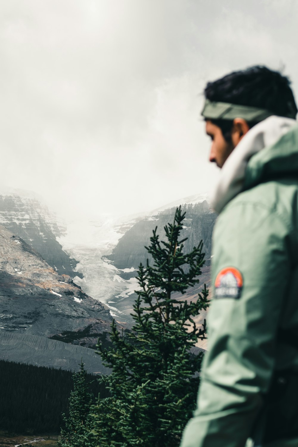 man in green jacket standing near green trees and mountain during daytime