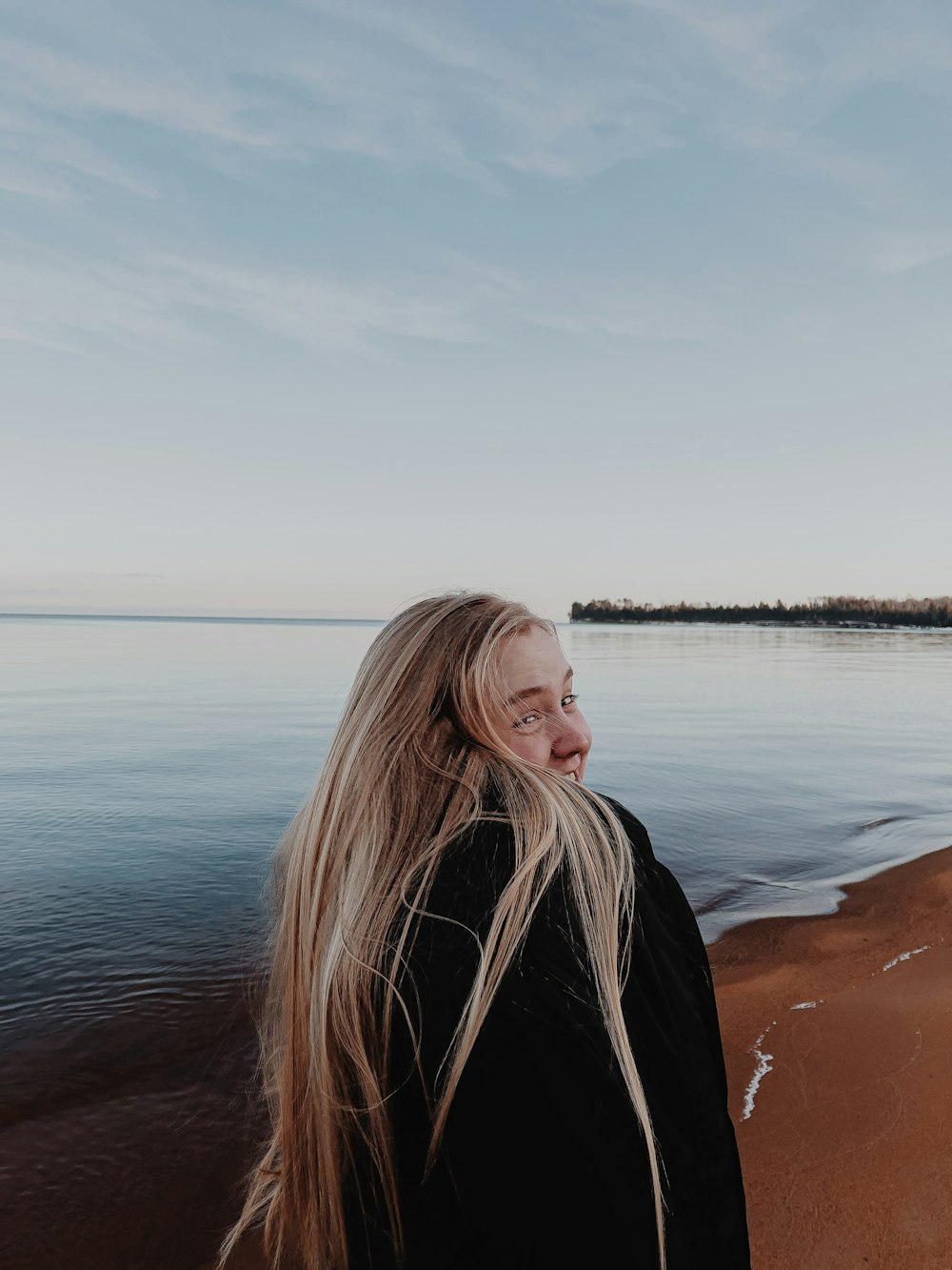 woman in black jacket standing on brown sand near body of water during daytime