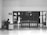 A person sits at a desk with a computer in a mostly empty room, which features a large wooden door with several posted notices and signs. A sign on the wall indicates 'Visitor report to security'. The scene is captured in black and white, giving it a minimalist and somber appearance.