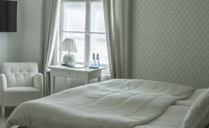 A serene bedroom with natural light streaming through large windows, adorned with soft linens.