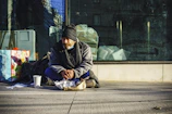 man in black and gray jacket sitting on sidewalk during daytime