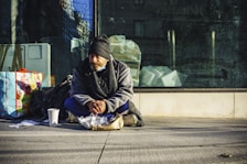 man in black and gray jacket sitting on sidewalk during daytime