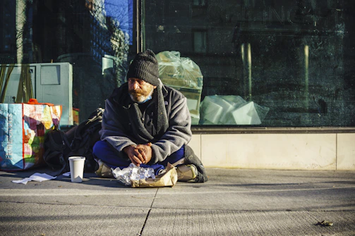 man in black and gray jacket sitting on sidewalk during daytime