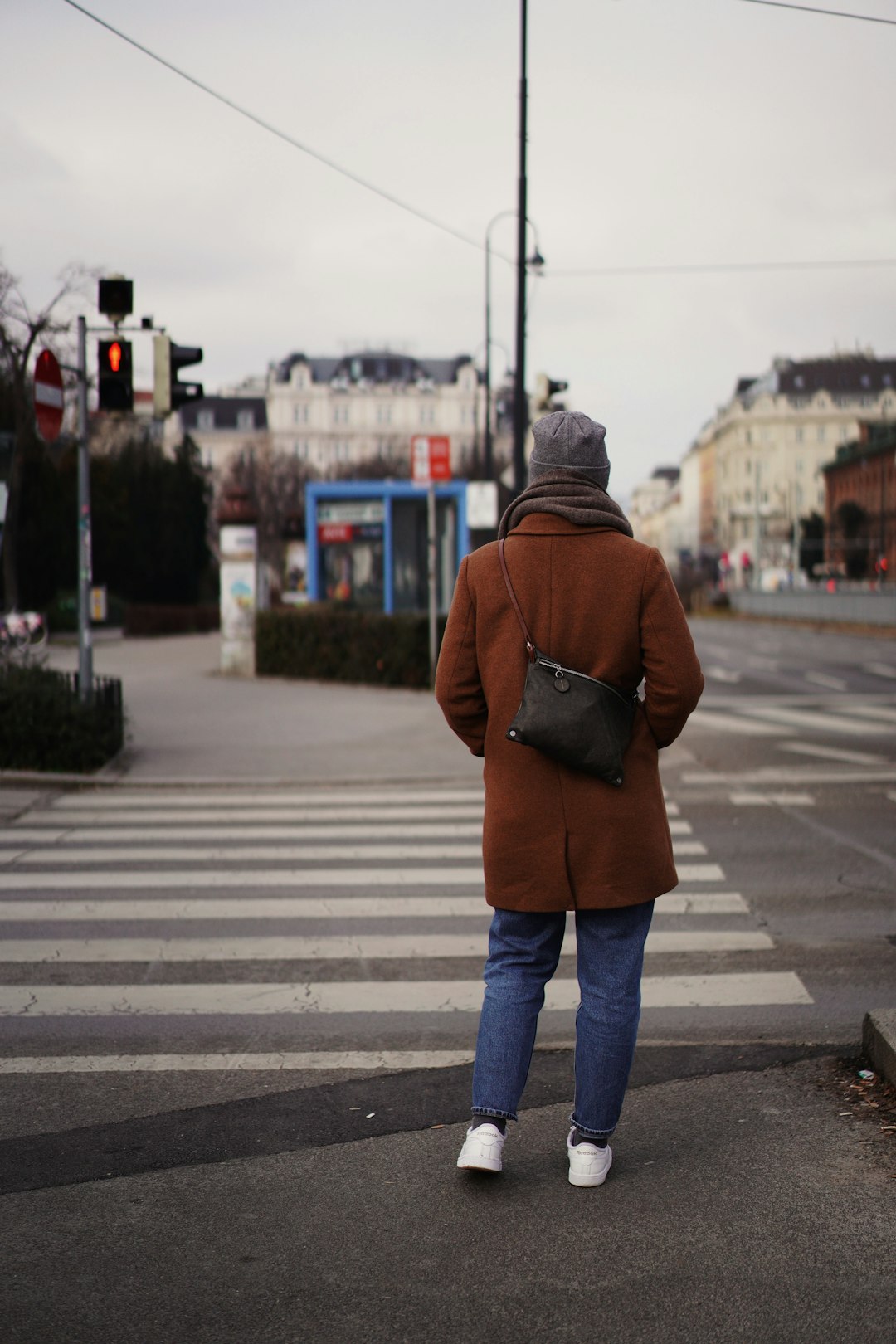 woman in brown jacket and blue denim jeans walking on pedestrian lane during daytime