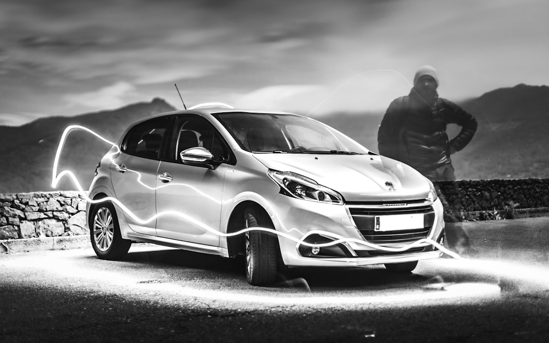 grayscale photo of man standing beside car