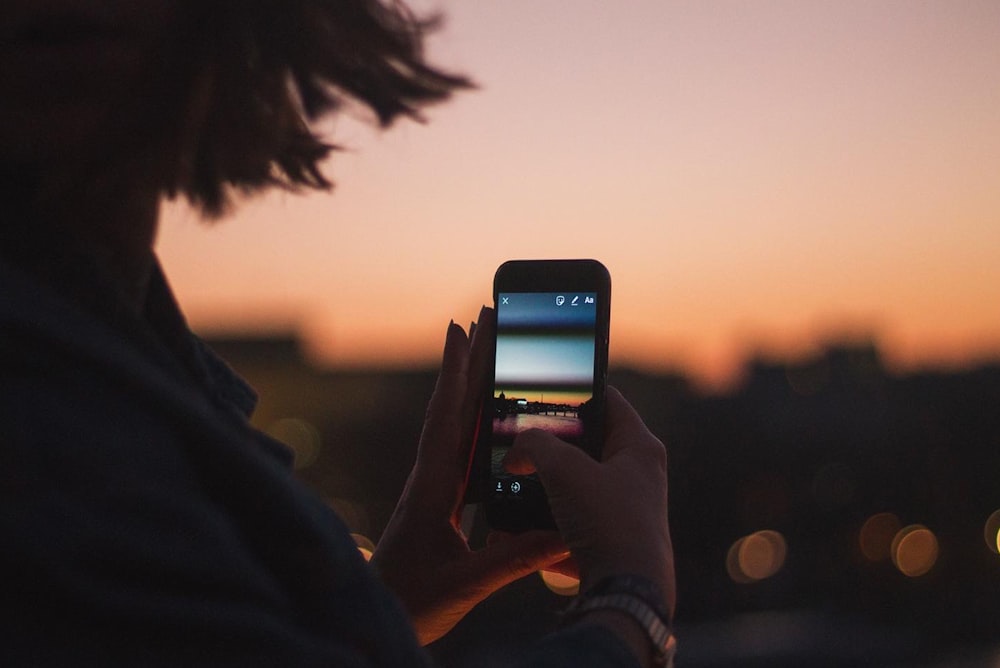 Persona sosteniendo iPhone 6 tomando foto de la puesta de sol