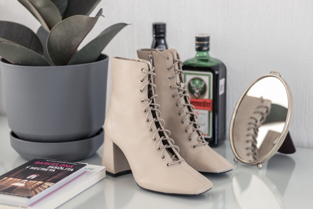 white leather boots beside green glass bottle