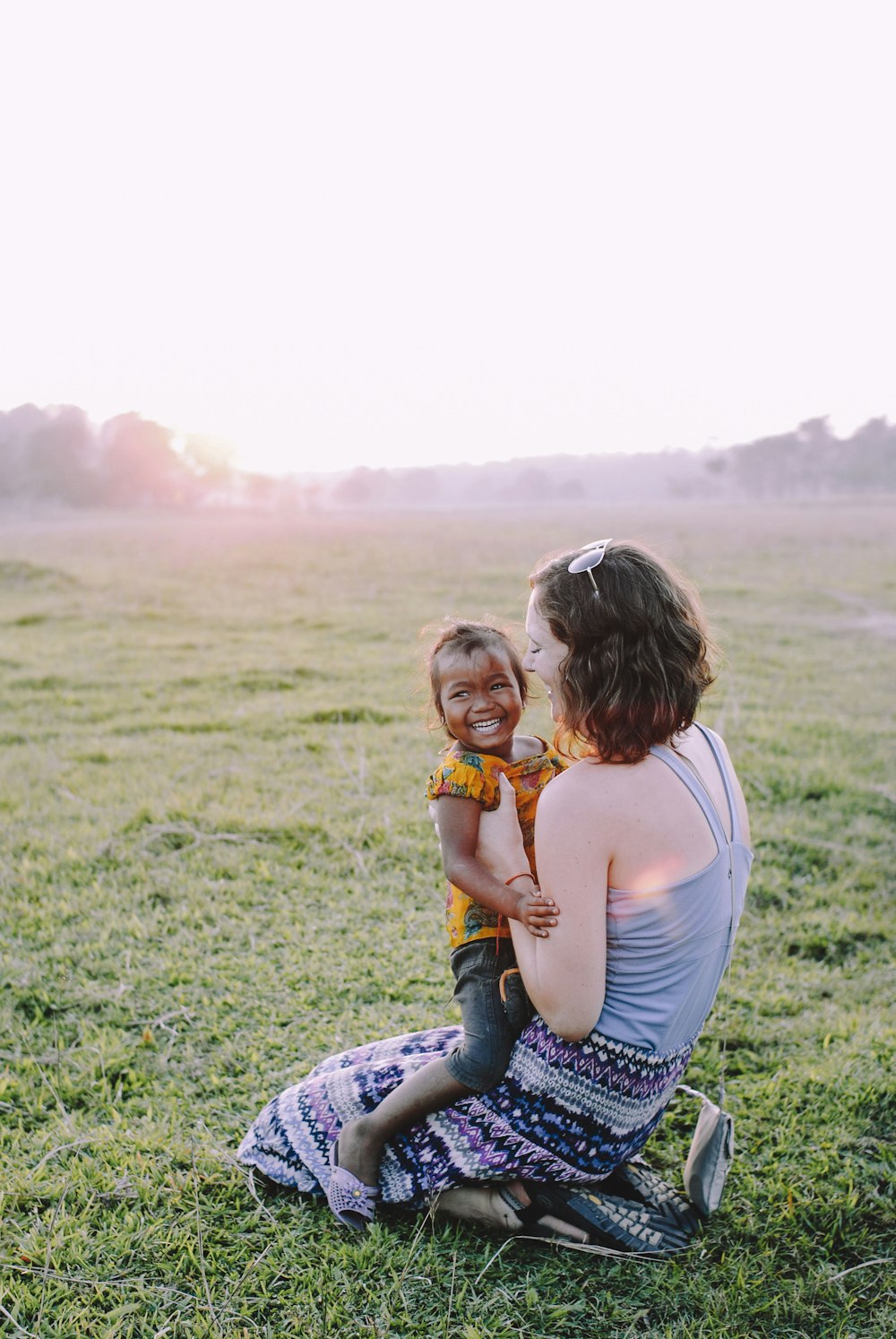 woman in white tank top and blue denim jeans sitting on green grass field during daytime