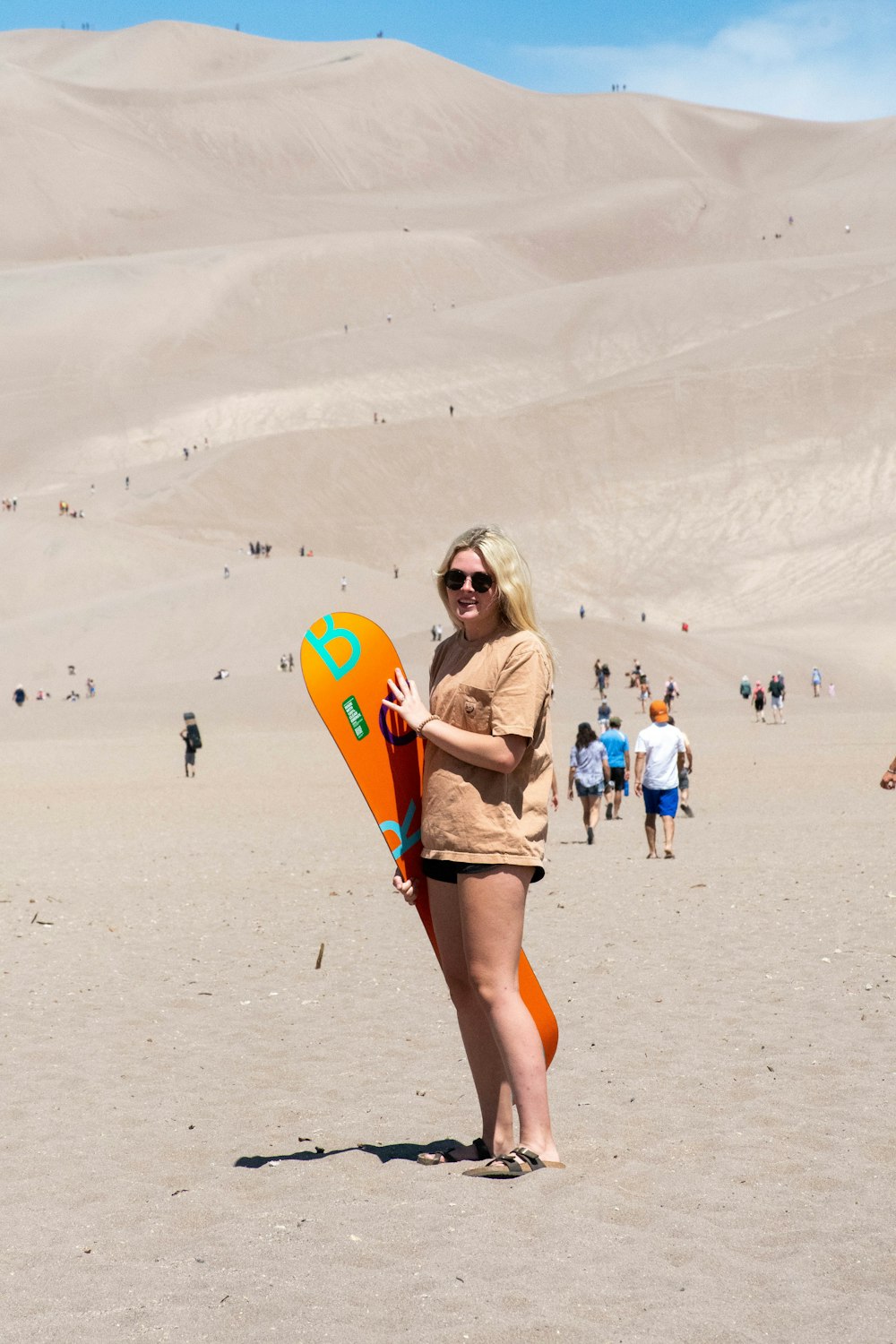 woman in white shirt and blue denim shorts holding orange and yellow surfboard on white sand