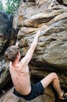 topless boy climbing on brown rock formation during daytime