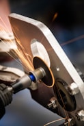 A metal grinding process where sparks are flying as a circular grinding tool is working on a piece of metal. The scene appears to be in a workshop setting with detailed focus on the machine and the metal piece.
