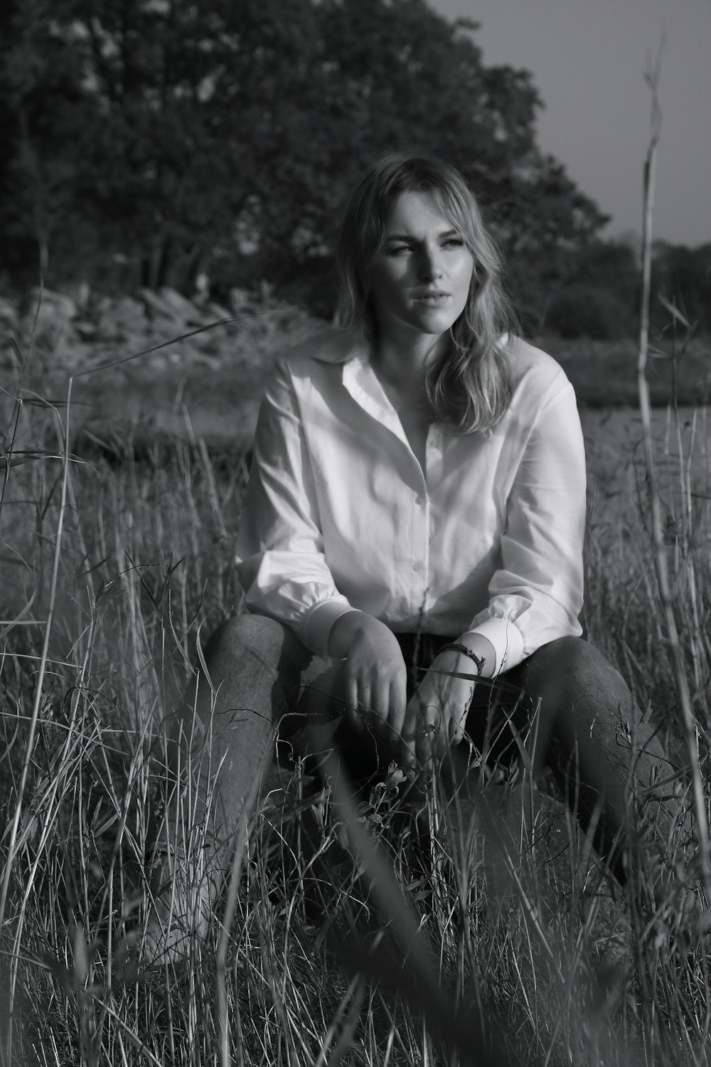 grayscale photo of woman in long sleeve shirt sitting on grass