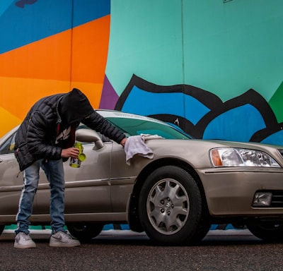 man in black jacket and blue denim jeans standing beside silver car