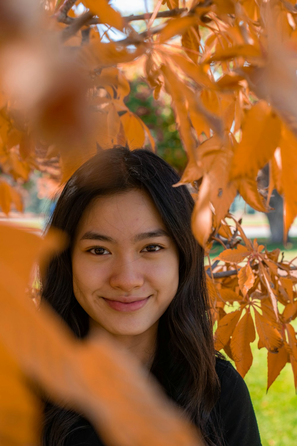 donna sorridente vicino alle foglie marroni durante il giorno
