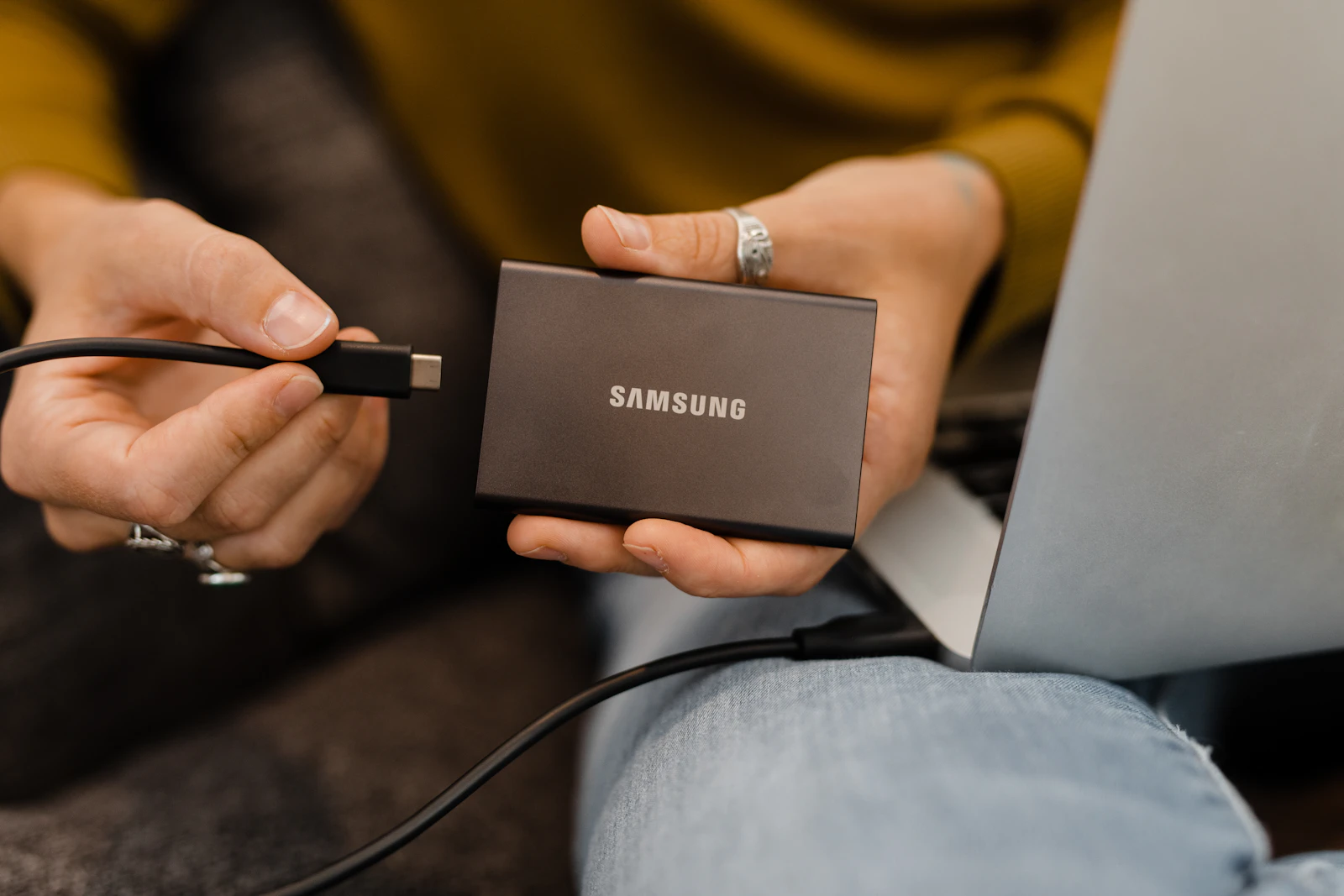 Person holding a black portable SSD beside a laptop