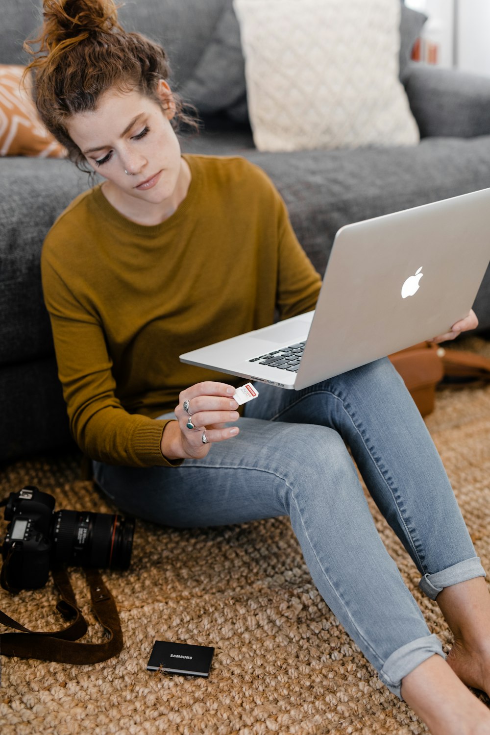 woman in green long sleeve shirt and blue denim jeans sitting on brown carpet using macbook