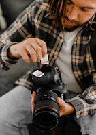 man in white and blue plaid dress shirt holding black nikon dslr camera