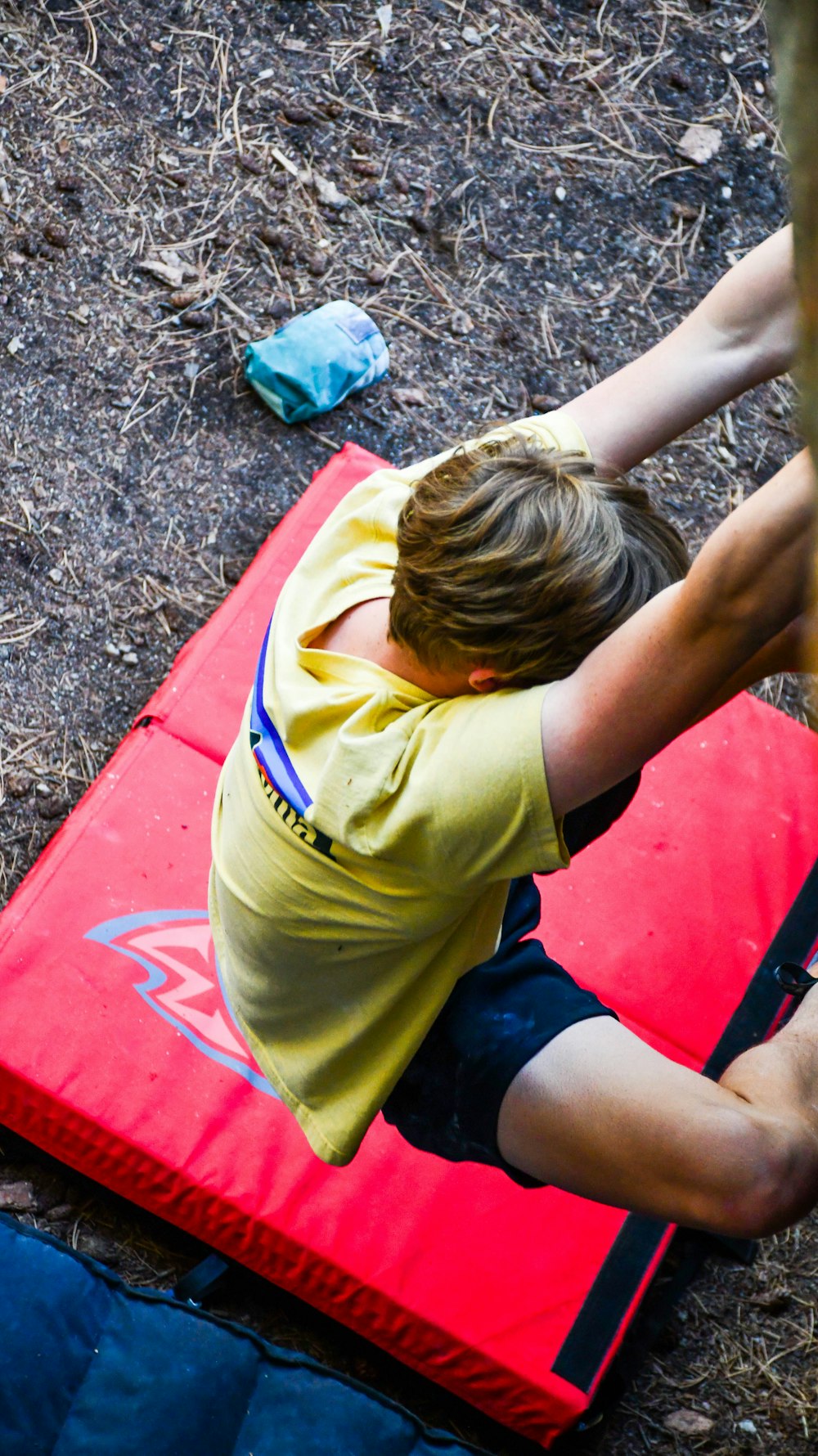 boy in yellow t-shirt and blue shorts sitting on red kayak