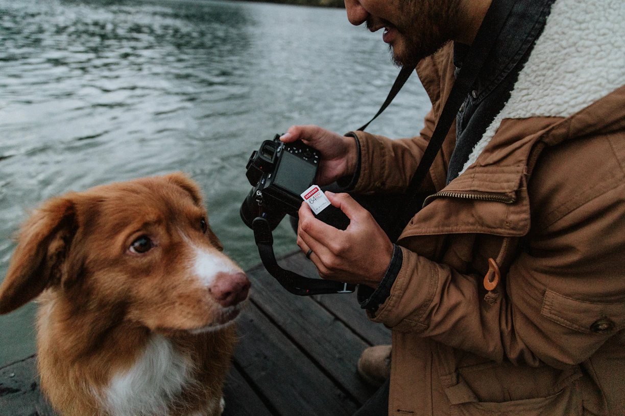 person in brown jacket holding black dslr camera beside brown and white short coated dog