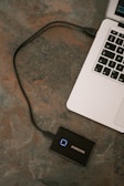 A laptop is connected to a Samsung external solid-state drive via a USB cable. The laptop's keyboard is partially visible on a textured surface.