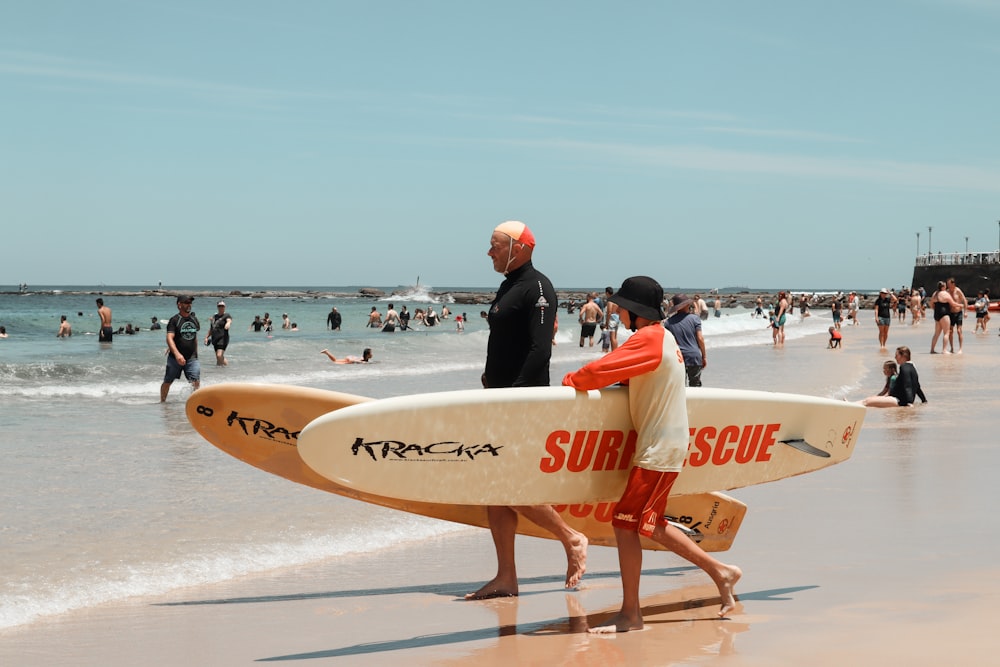 homem em traje de mergulho preto segurando prancha de surf branca andando na praia durante o dia