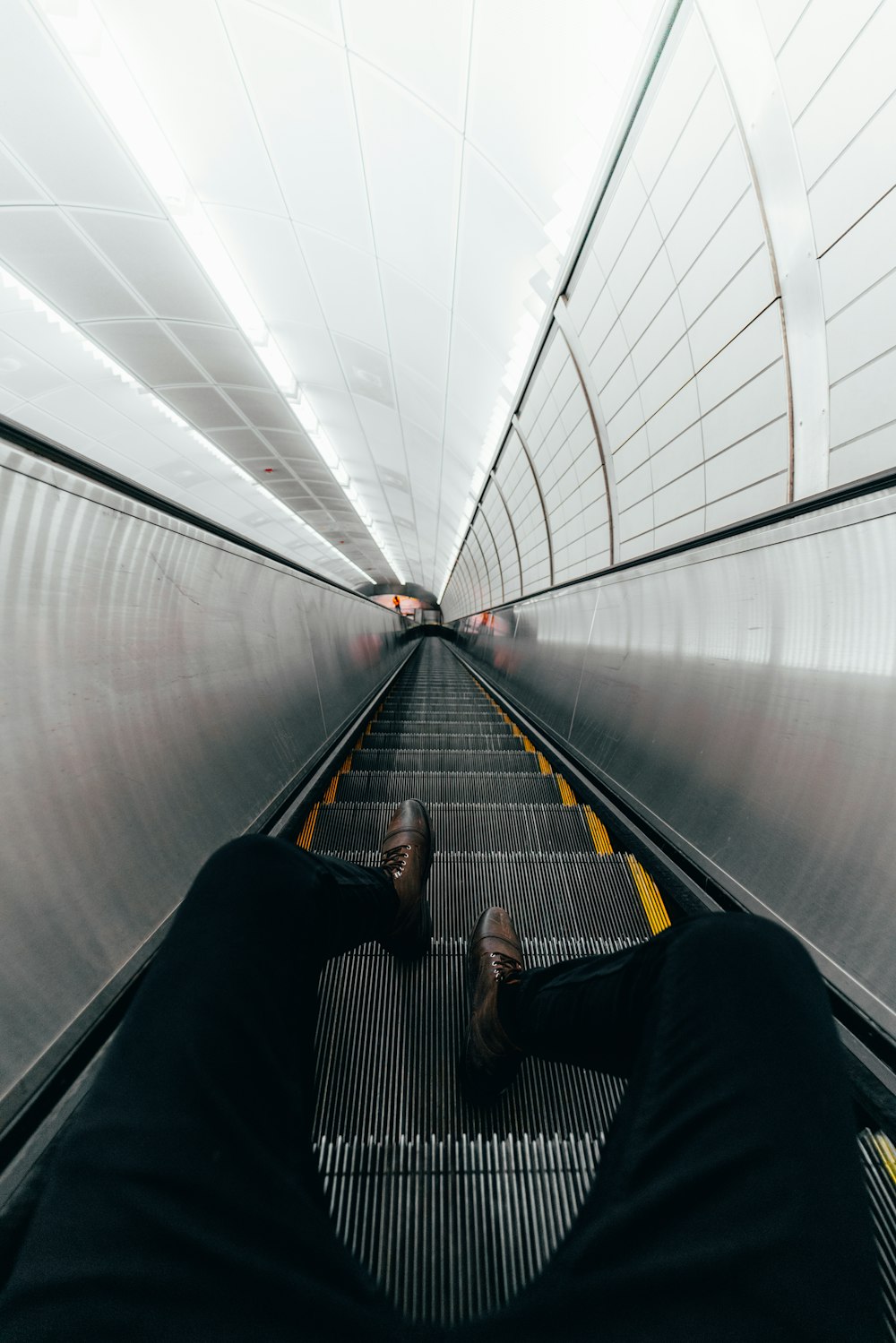 man in black jacket and black pants walking on escalator