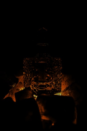 A dark, atmospheric setting features a textured glass bottle surrounded by chunks of translucent ice. The dim lighting casts a warm, amber glow, highlighting the intricate designs of the glass and creating dramatic shadows.