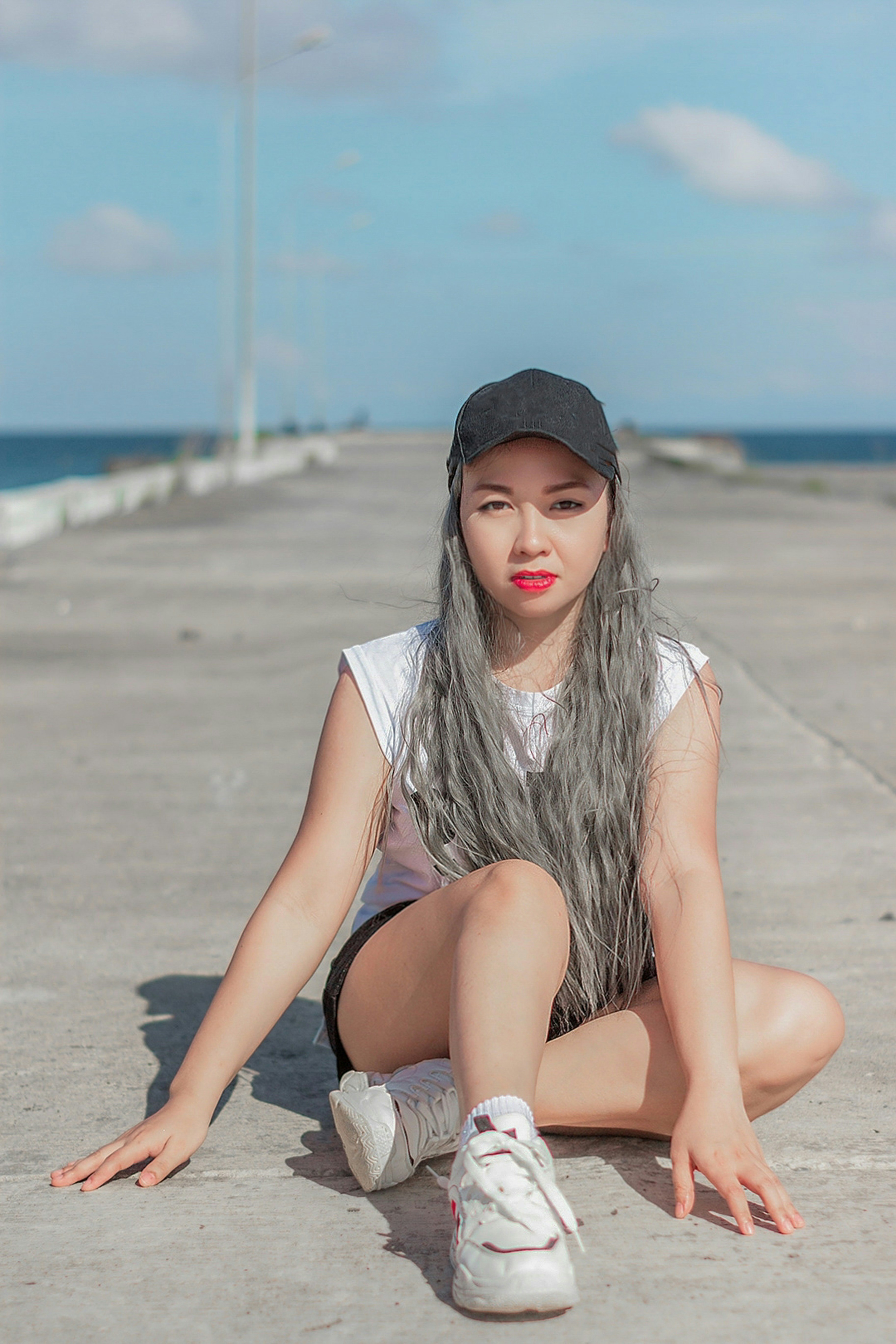 Wanita dengan kemeja putih dan celana pendek hitam duduk di pantai di siang hari