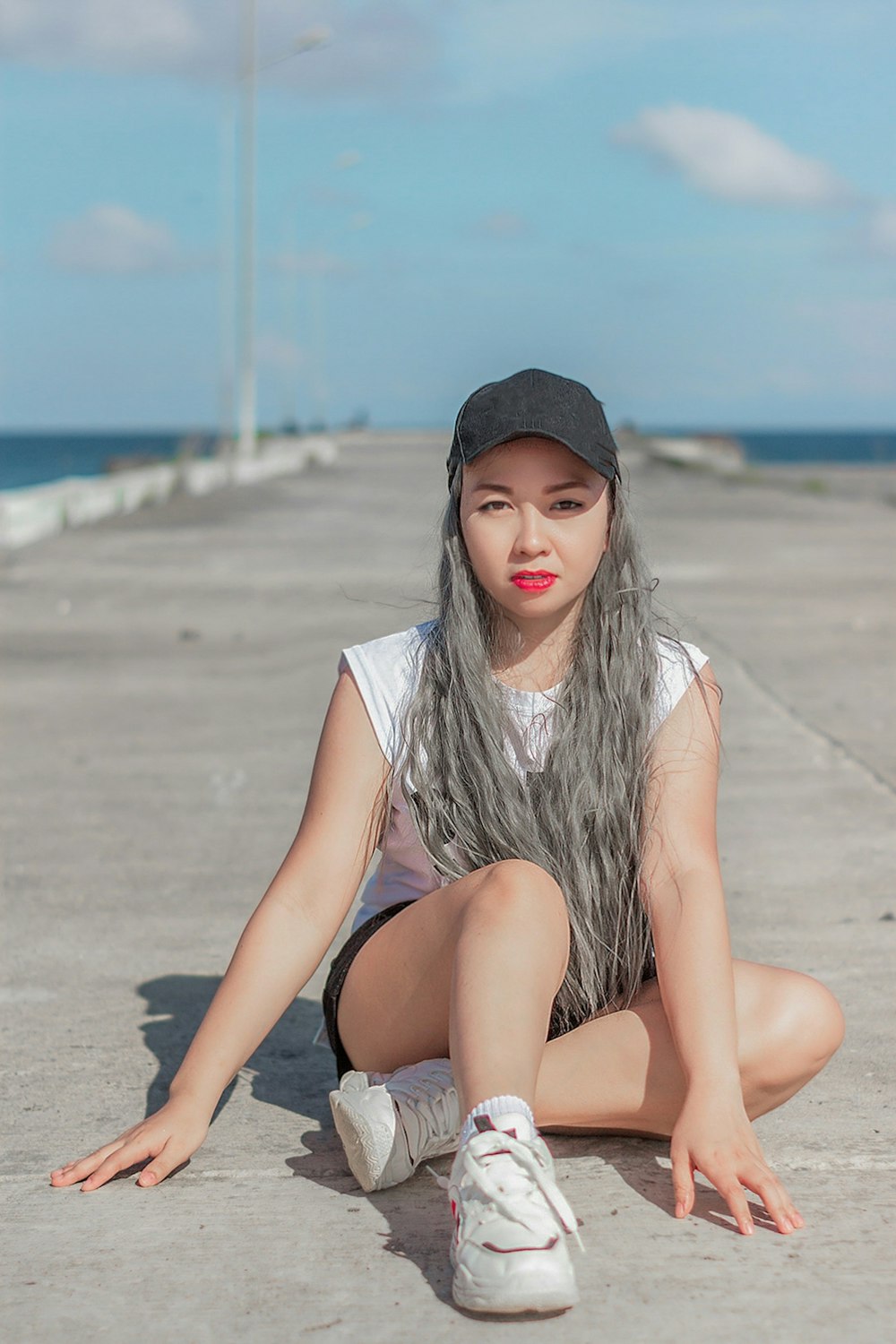 woman in white shirt and black shorts sitting on beach during daytime