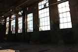 Sunlight streaming through shattered glass in an old, empty factory hall.