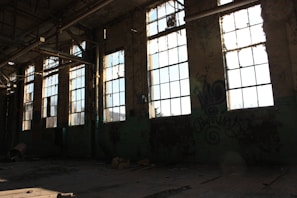 Sunlight streaming through shattered glass in an old, empty factory hall.