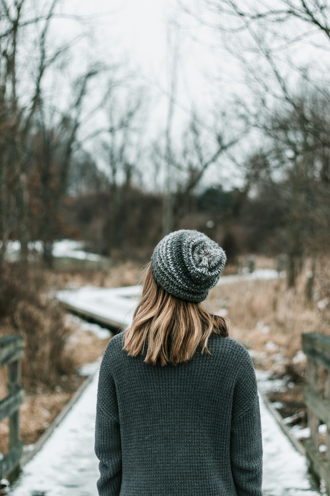 woman in gray knit cap and gray sweater standing near bare trees during daytime