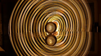 A mesmerizing display of concentric golden light rings emanates from a central point, creating a tunnel-like illusion. The lights reflect on a smooth surface below, enhancing the symmetrical and hypnotic effect.