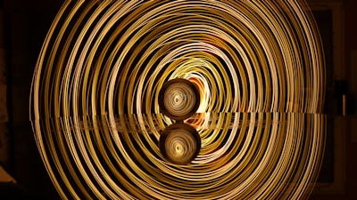 A mesmerizing display of concentric golden light rings emanates from a central point, creating a tunnel-like illusion. The lights reflect on a smooth surface below, enhancing the symmetrical and hypnotic effect.