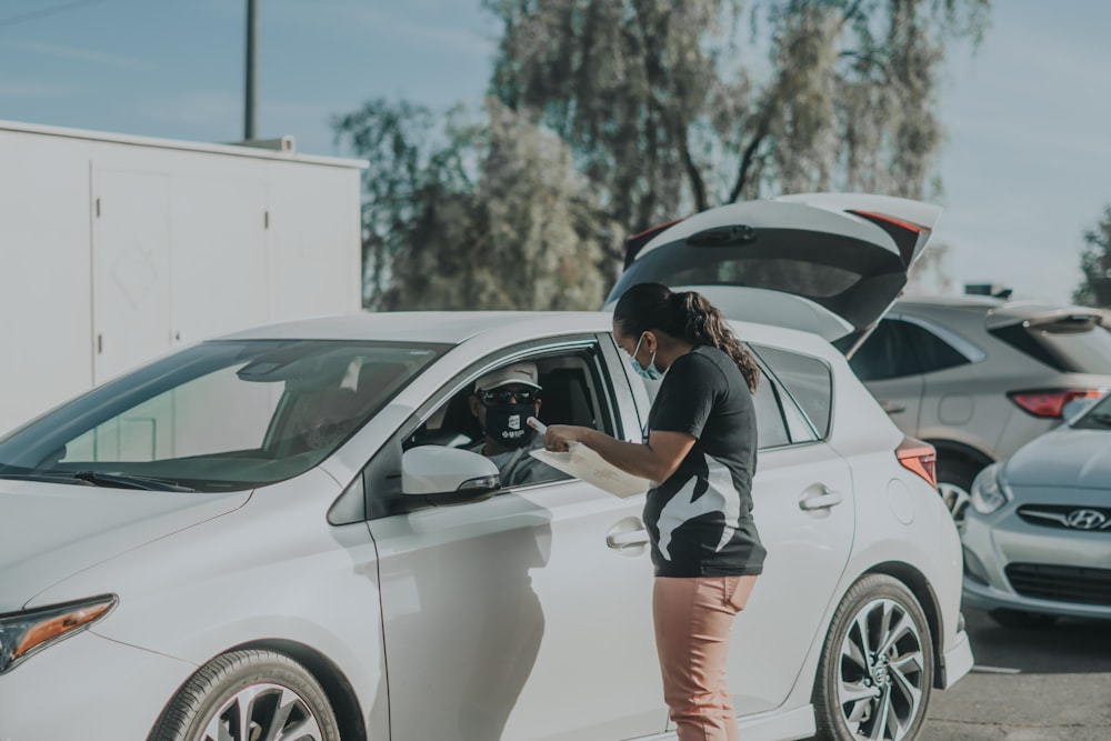 woman in black and white shirt and orange shorts leaning on white car during daytime