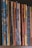 A row of vertically arranged magazines or booklets with varying colorful covers and visible spines lined up side by side. The collection exhibits a mixture of patterns and designs, with some covers worn and slightly bent, indicating frequent handling.