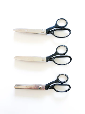 Rows of industrial scissors lined up on a sleek metallic workbench, highlighting their polished edges.