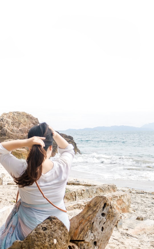 woman in white long sleeve shirt standing on rock formation near sea during daytime in Lampung Indonesia