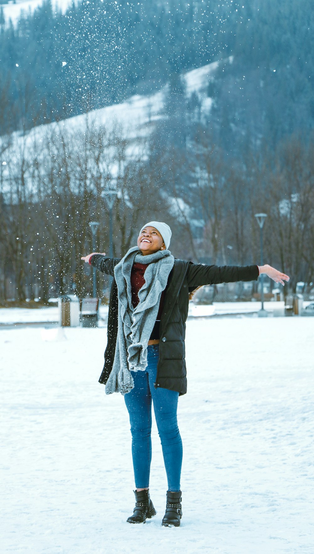 昼間、雪に覆われた地面に立つ黒いジャケットとブルーデニムジーンズの女性