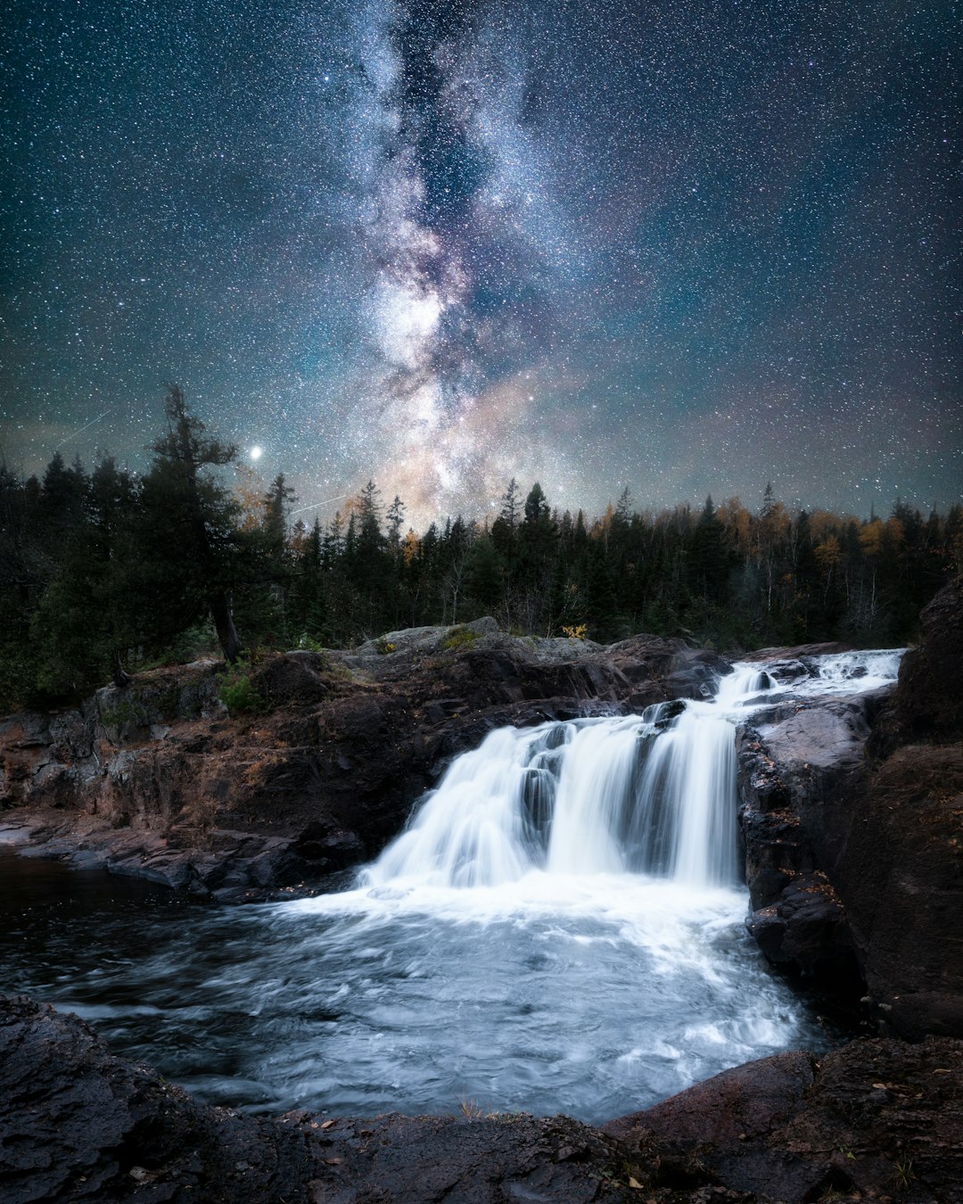 waterfalls near green trees under blue sky during night time