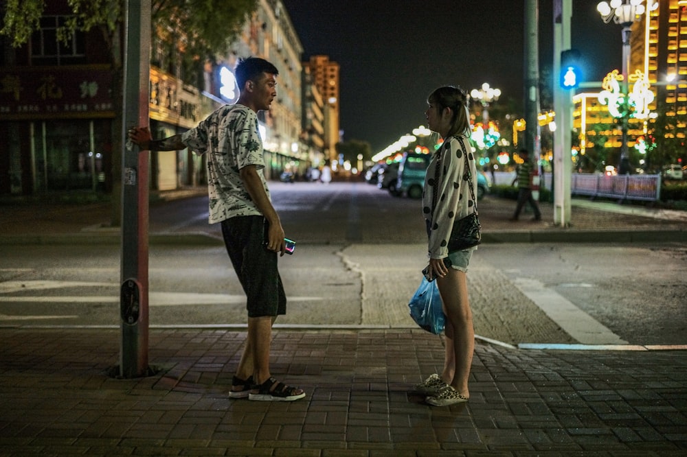 man in white and black plaid shirt walking on sidewalk during night time