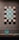 A display of intricately designed tiles with geometric and floral patterns. The tiles are arranged in a symmetrical pattern on a wall, featuring a blend of turquoise and earthy tones. A leaf-shaped ceramic ornament sits on a stand below, matching the tiles' color scheme.