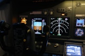 The image features the cockpit of an aircraft, displaying various control panels, illuminated instruments, dials, and screens showing flight data. Visible are the yoke and multiple indicators for navigation and system status, with labels and lights.