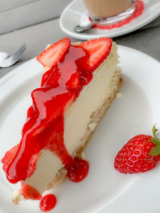 A close-up of a creamy New York-style cheesecake with a golden crust and a fresh strawberry topping.