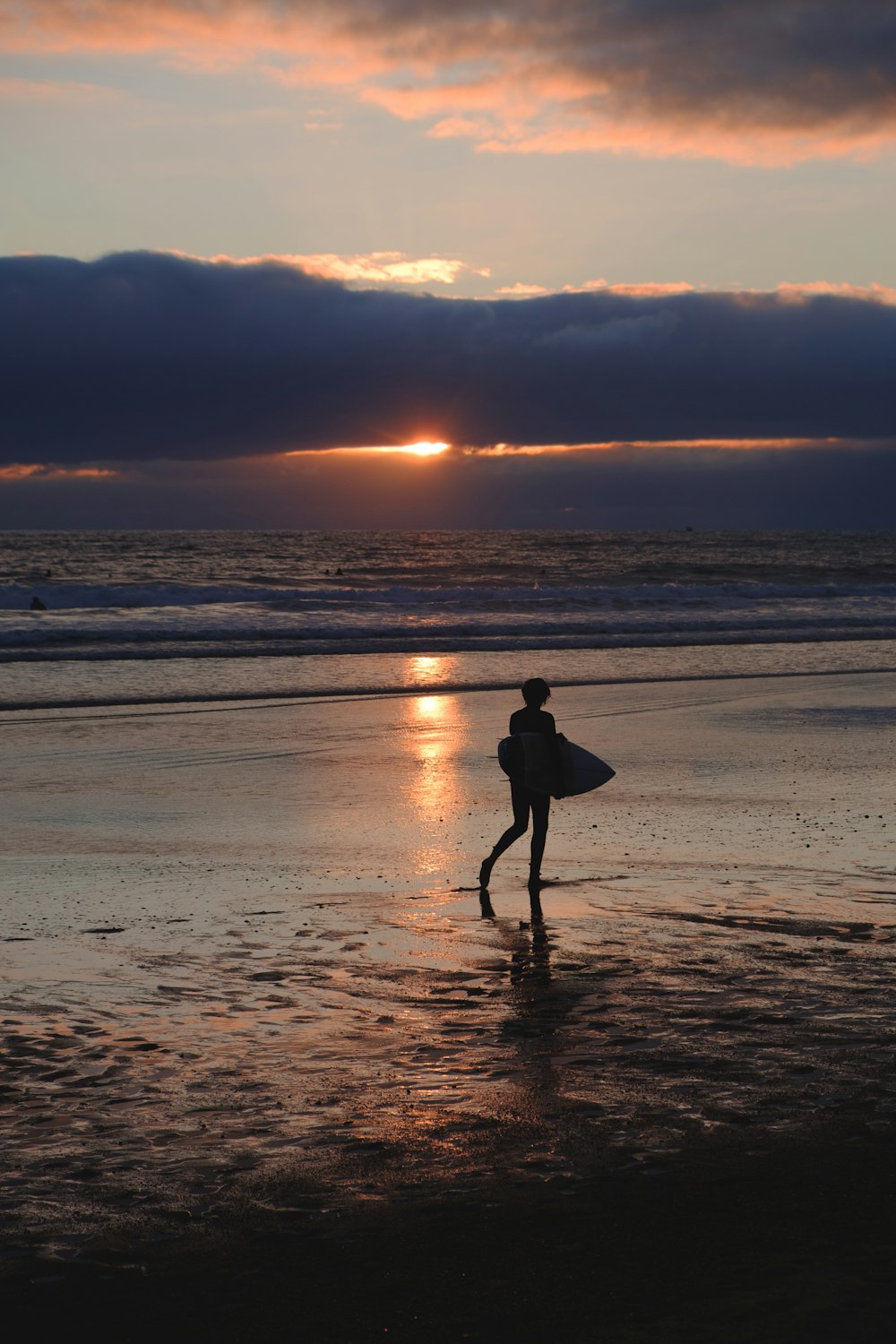 silhouette of person holding surfboard walking on beach during sunset