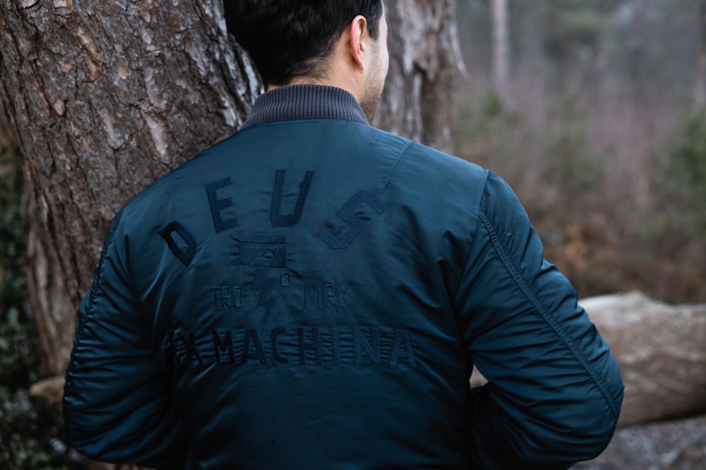 man in blue long sleeve shirt leaning on brown tree