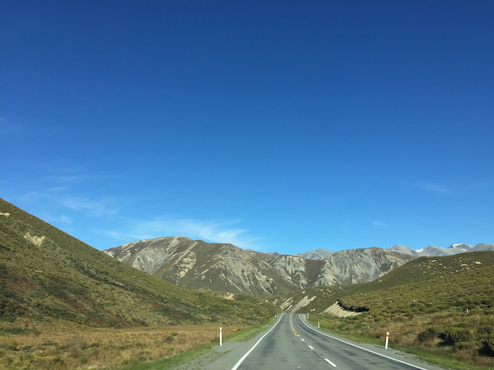 gray asphalt road near green grass field and mountains under blue sky during daytime