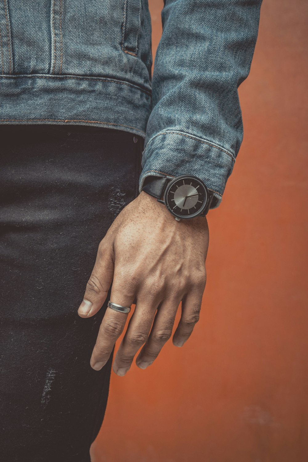 person in blue denim jacket wearing black leather strap round analog watch