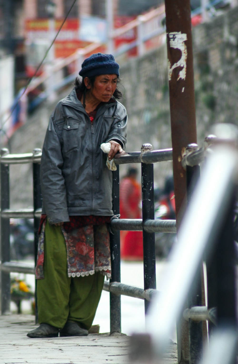 woman in gray jacket standing beside brown metal fence during daytime