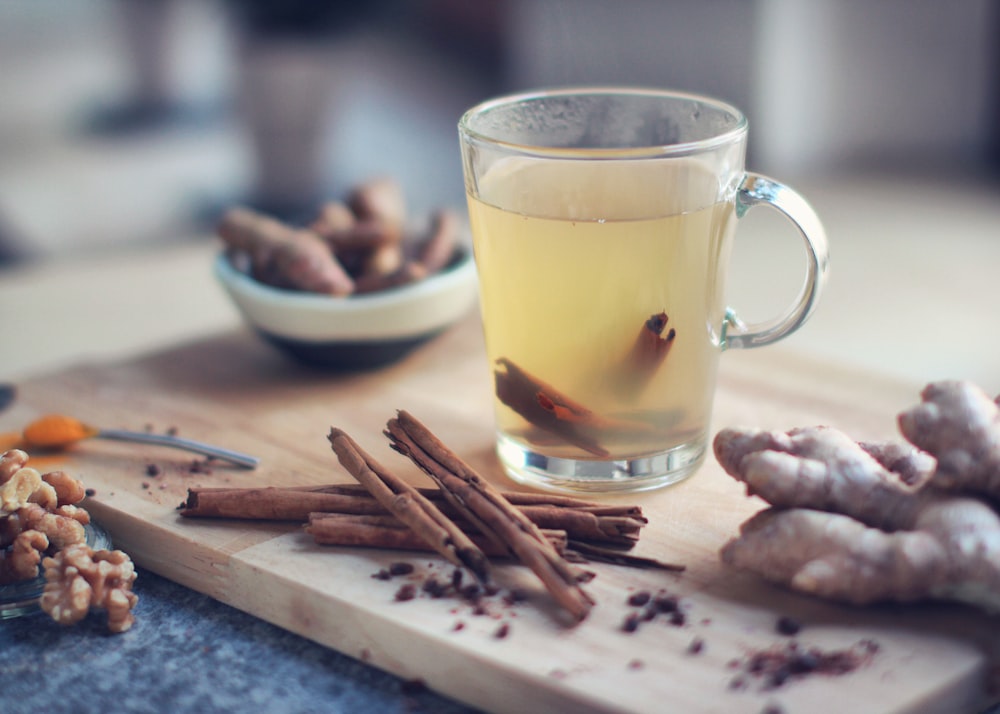 Taza de vidrio transparente con líquido amarillo sobre tabla de cortar de madera marrón